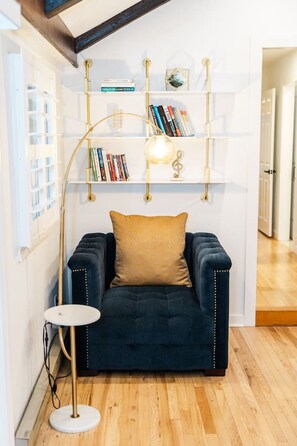 A cozy reading nook with a dark blue armchair, a round white side table, and a gold floor lamp.