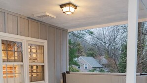 A hot tub on a wooden deck with a covered porch, a window with a view of a house, and a ceiling light fixture. - Cowry Acres - The First House Villa w Hot Tub (New Hope)