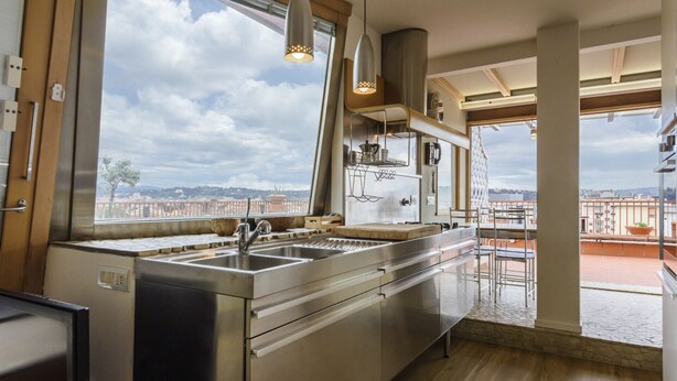 Una cocina moderna con una isla grande, electrodomésticos de acero inoxidable y vistas de la ciudad a través de amplios ventanales.
