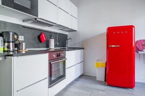 Une cuisine moderne avec des meubles blancs, un réfrigérateur rouge, des appareils en acier inoxydable et un plan de travail noir.