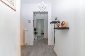 A hallway with a radiator, a potted plant, a chandelier, and a shelf with decorative items.