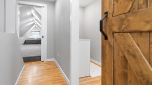 A narrow hallway with wooden flooring leading to a bedroom with a sloped ceiling and a bed. - Newly Remodeled Downtown Helena Home, Sleeps 11 (Helena)