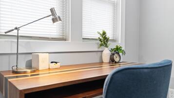 Un escritorio de madera con una lámpara, un jarrón blanco con una planta y un despertador antiguo.