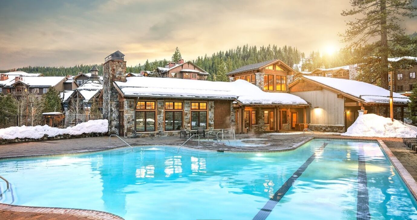 A resort with a swimming pool, stone buildings, and snow-covered roofs.