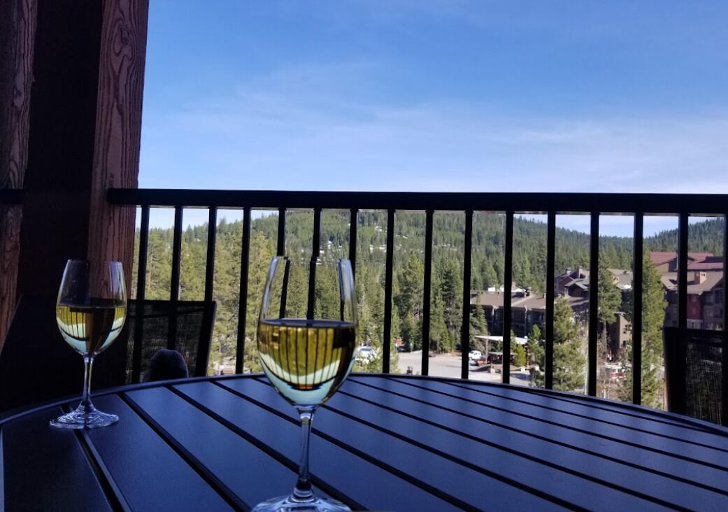 Deux verres de vin blanc sur une table, avec vue sur une chaîne de montagnes boisées.