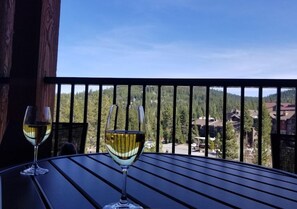 Dos copas de vino blanco sobre una mesa con vistas a una cadena montañosa boscosa.