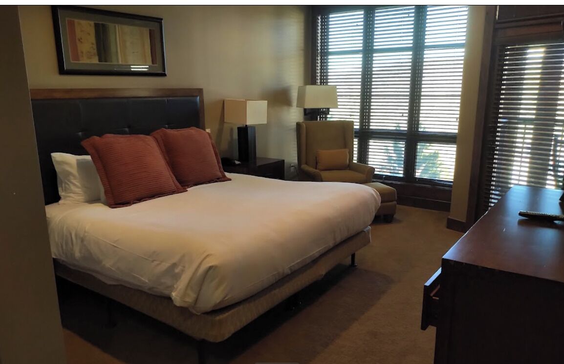 A hotel room with a large bed, two bedside lamps, a chair, and a desk.