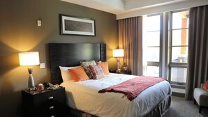 Une chambre d’hôtel avec un grand lit, deux tables de chevet avec des lampes, un tableau encadré au mur et une fenêtre avec des rideaux.