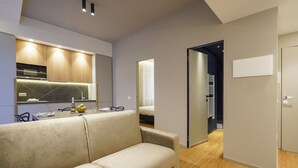 Un salon moderne comprenant un canapé, une table à manger avec des chaises, un coin cuisine avec une cuisinière et des placards, et un couloir menant à une chambre.