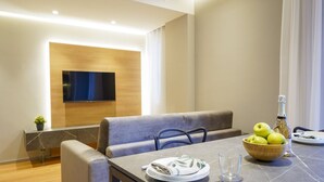 Un espace repas moderne avec un téléviseur à écran plat fixé au mur, un banc rembourré, une table en marbre et un saladier rempli de pommes.