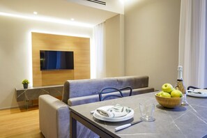 A modern dining area with a flat-screen TV mounted on the wall, a cushioned bench, a marble table, and a bowl of apples. - GuestHost - Eleanto Apartment a stone's throw from the sea (Trani)