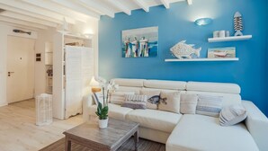 A living room with a white sofa, a coffee table, and a blue accent wall. - GuestHost - Cozy studio with loft of 70 square meters, able to accommodate up to 6 people, located on the third floor of a building without elevator in the heart of Sanremo. The property is equipped with every comfort and a plus is definitely the furnish (Sanremo)