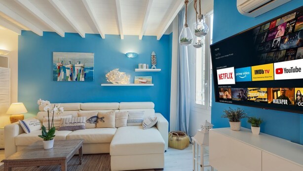 A living room with a blue wall, white sofa, and a mounted TV displaying streaming services. - GuestHost - Cozy studio with loft of 70 square meters, able to accommodate up to 6 people, located on the third floor of a building without elevator in the heart of Sanremo. The property is equipped with every comfort and a plus is definitely the furnish (Sanremo)