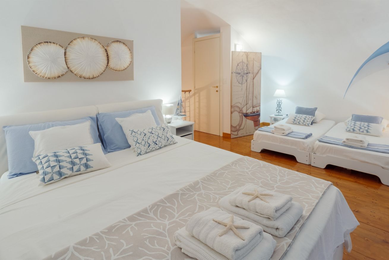 Habitación de hotel con una cama grande, dos camas más pequeñas, una obra de arte con temática náutica y una escalera que conduce a otra habitación.