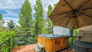 A wooden deck with a hot tub, outdoor furniture, and a view of trees.