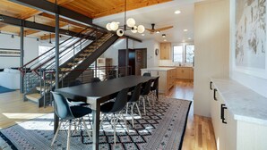 A modern kitchen with a large island, wooden ceiling, and a staircase leading to an upper level.