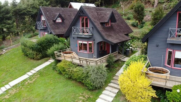 A cluster of two-story houses with balconies, surrounded by lush greenery and a wooden deck. - CIPRES Ecolodge & Spa (Frutillar)