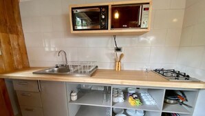 A kitchen with a wooden countertop, a built-in microwave, a gas stove, and shelves with dishes and utensils. - CIPRES Ecolodge & Spa (Frutillar)