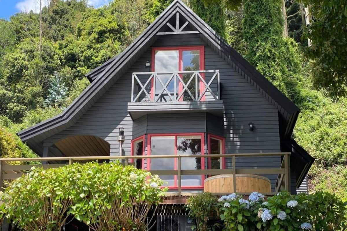 Een chalet met balkon, een raam met rode omlijsting en een houten terras.