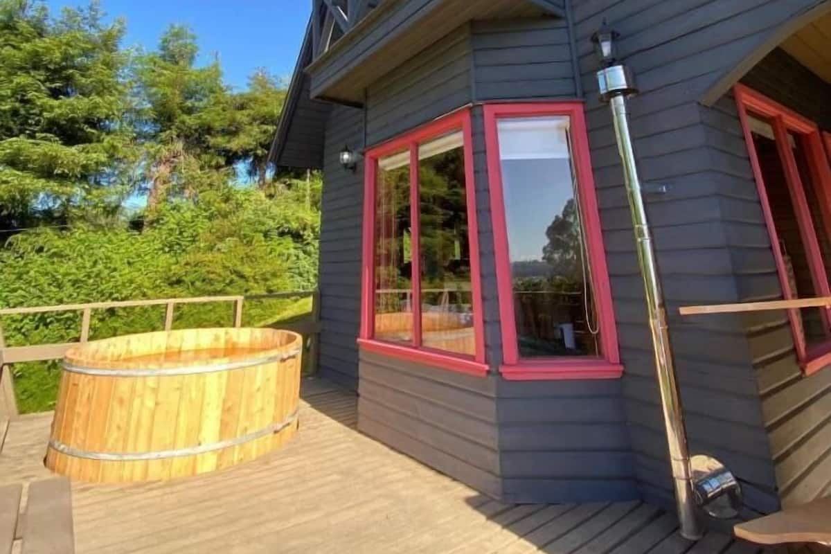 Een gebouw met twee verdiepingen, een houten terras, een jacuzzi en een balkon met rode sierlijsten.
