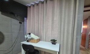 Une piÚce avec un bureau blanc, une petite plante, une serviette enroulée et un rideau.