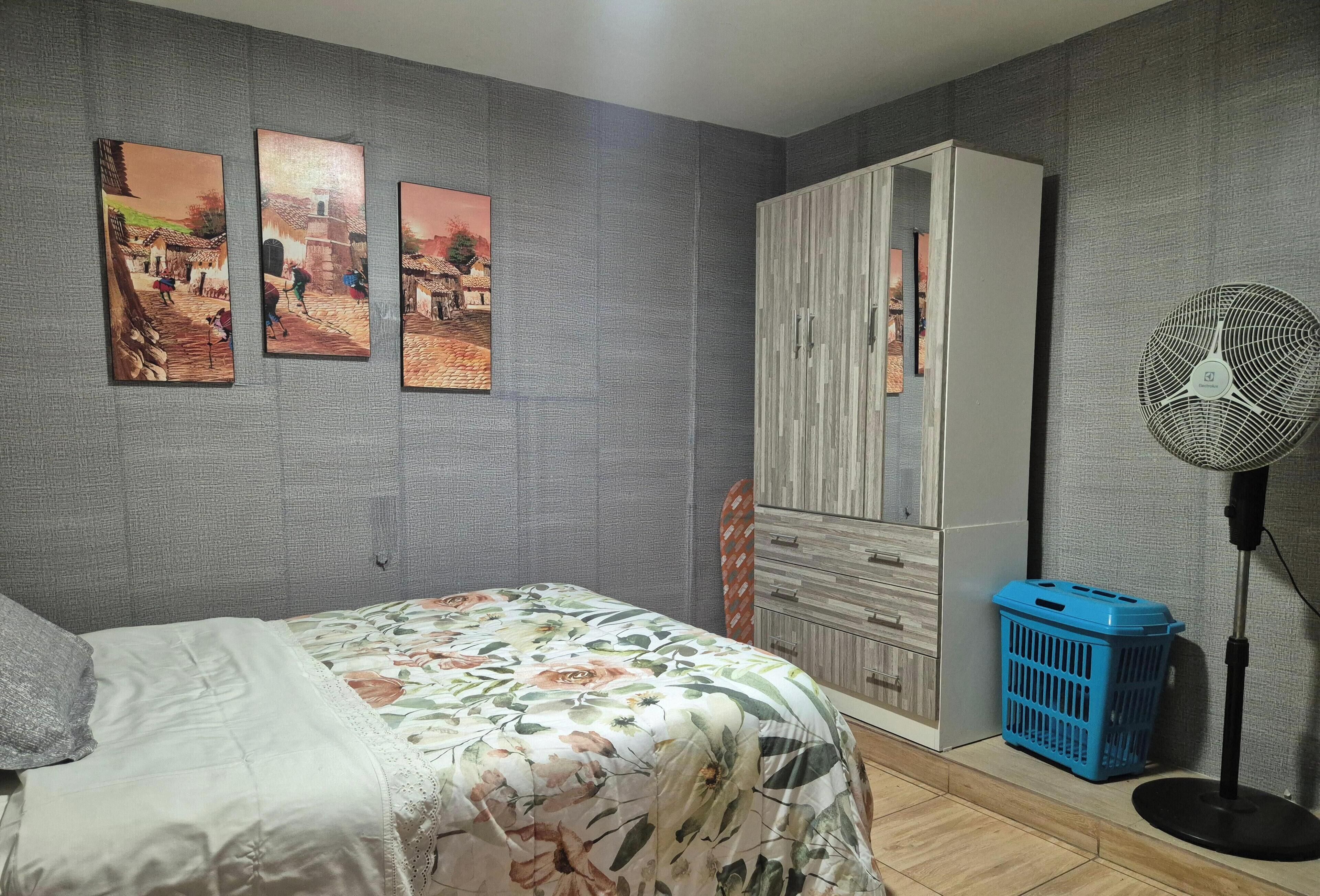 Un dormitorio con cama, armario, ventilador y tres cuadros en la pared.