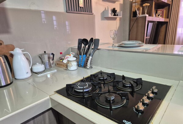 A kitchen with a gas stove, kettle, coffee maker, and utensils.