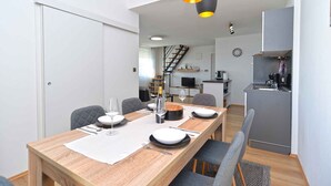 Un comedor moderno con una mesa de madera preparada para cuatro personas, una cocina al fondo y una escalera que sube a un nivel superior.