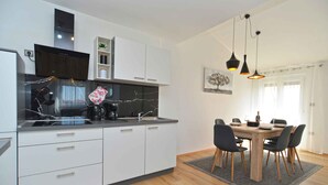 Una cocina moderna con armarios blancos, un salpicadero de mármol negro y un comedor con mesa y sillas de madera.