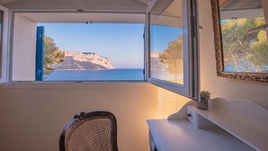 Ein Zimmer mit Blick auf eine Klippe und das Meer, ein Sessel und ein kleiner Tisch mit einer Pflanze.