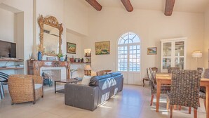 Ein geräumiges Wohnzimmer mit Kamin, einem großen Spiegel und einer Essecke mit Korbstühlen.