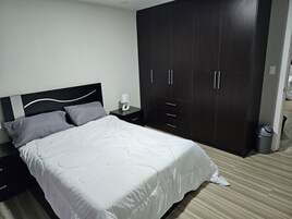 Quarto com cama, mesas de cabeceira, guarda-roupa e lixeira.