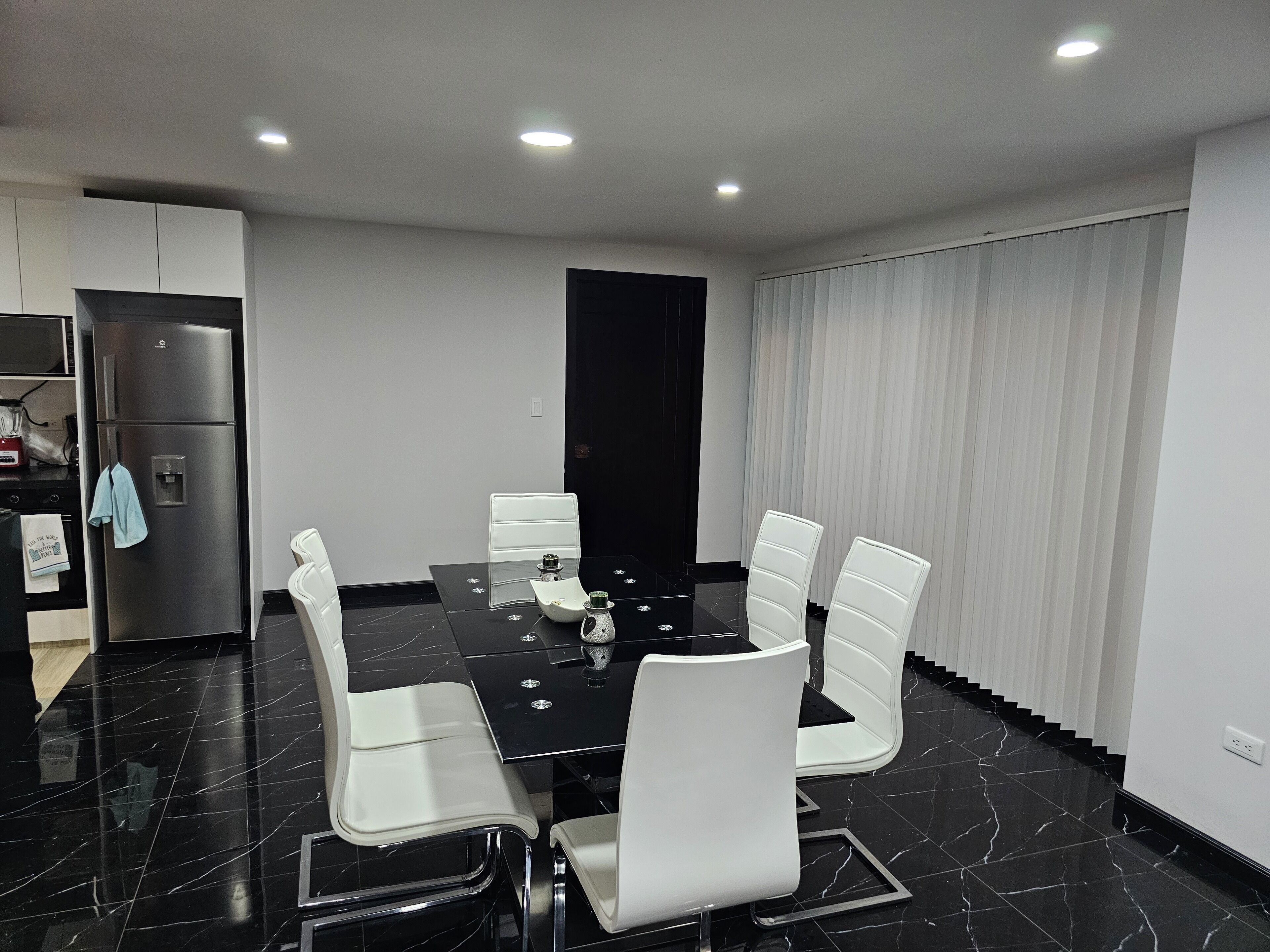 A modern dining area with a black marble table, white chairs, and a black cabinet.