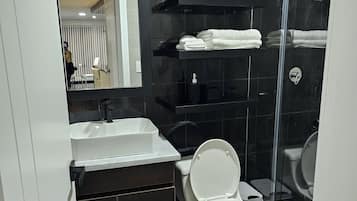 Un baño moderno con un lavabo blanco, un inodoro, cabina de ducha de vidrio y un espejo que refleja una pared a rayas y una puerta.