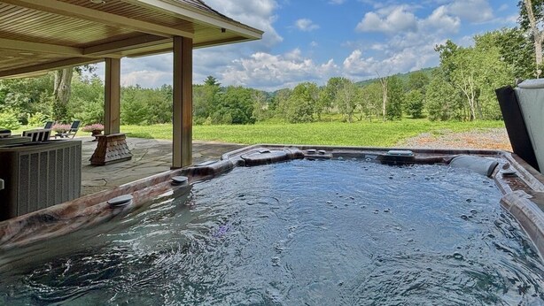 Ein Whirlpool mit Holzterrasse und Gartenmöbeln, eingebettet in eine üppige grüne Landschaft.