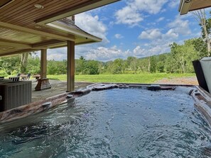 Ein Whirlpool mit Holzterrasse und Gartenmöbeln, eingebettet in eine üppige grüne Landschaft.