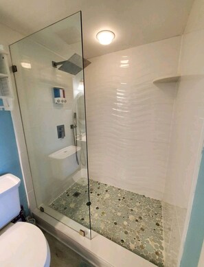 A glass-enclosed shower with a pebble-tiled floor, a white toilet, and a hand dryer.