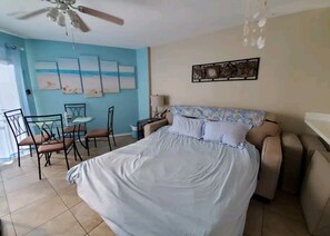 A bedroom with a bed, a ceiling fan, a dining table with chairs, and artwork on the walls.