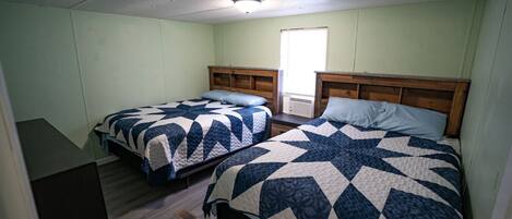 A room with two beds, each with a star-patterned quilt, wooden headboards, and a window providing natural light.