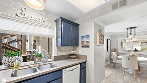 A modern kitchen with a built-in dishwasher, a large mirror, and a dining area with a chandelier. - Cozy Condo in the prestigious Ritz Pointe community STR23-0051 (Dana Point)