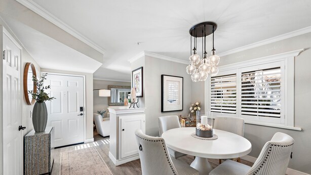 A dining area with a round table, striped chairs, a chandelier, and a window with blinds. - Cozy Condo in the prestigious Ritz Pointe community STR23-0051 (Dana Point)