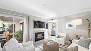A modern living room with a fireplace, white furniture, and a dining area with plants. - Cozy Condo in the prestigious Ritz Pointe community STR23-0051 (Dana Point)