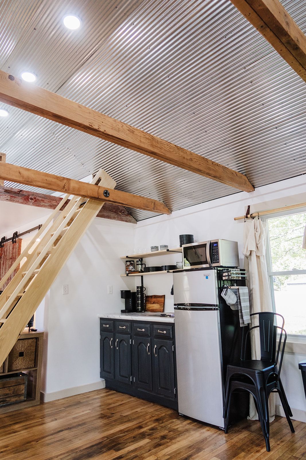 Una cocina compacta con microondas integrado, refrigerador y escalera de madera.