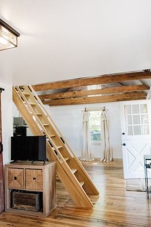 A room with a wooden staircase, a television on a cabinet, and a white door with glass panels.