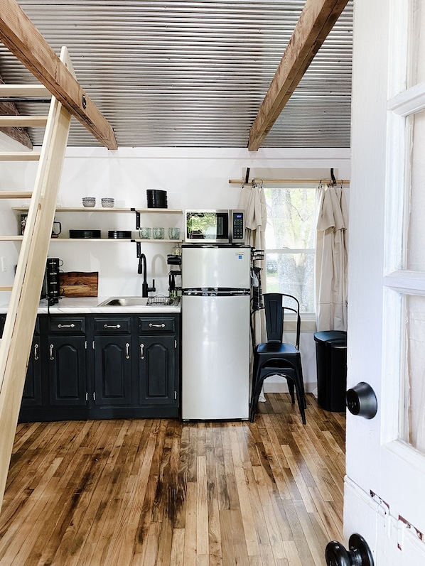 A compact kitchen with a white refrigerator, black cabinets, and a wooden ceiling.