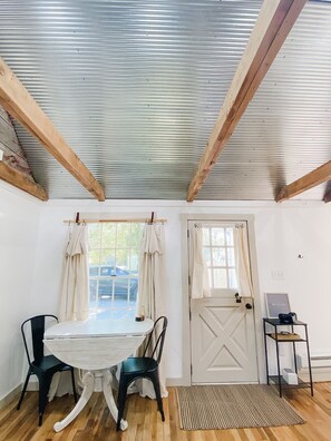 A room with a wooden ceiling, a white door, a table with two chairs, and a small side table with a sign.