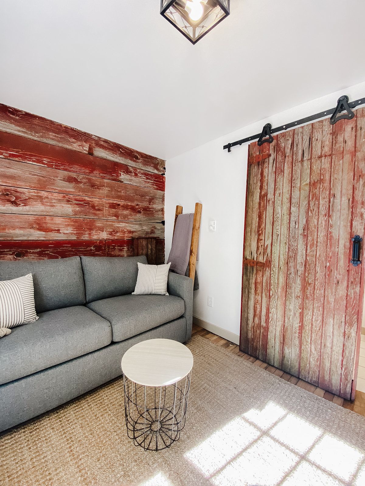 Une pièce avec un canapé gris, une table basse ronde, une porte en bois et un mur rouge à la texture particuli ère.