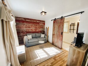 A living room with a grey sofa, a small round table, a wooden floor, and a red wooden wall.