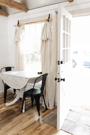 A room with a white table and chairs, a wooden floor, and a door leading outside.
