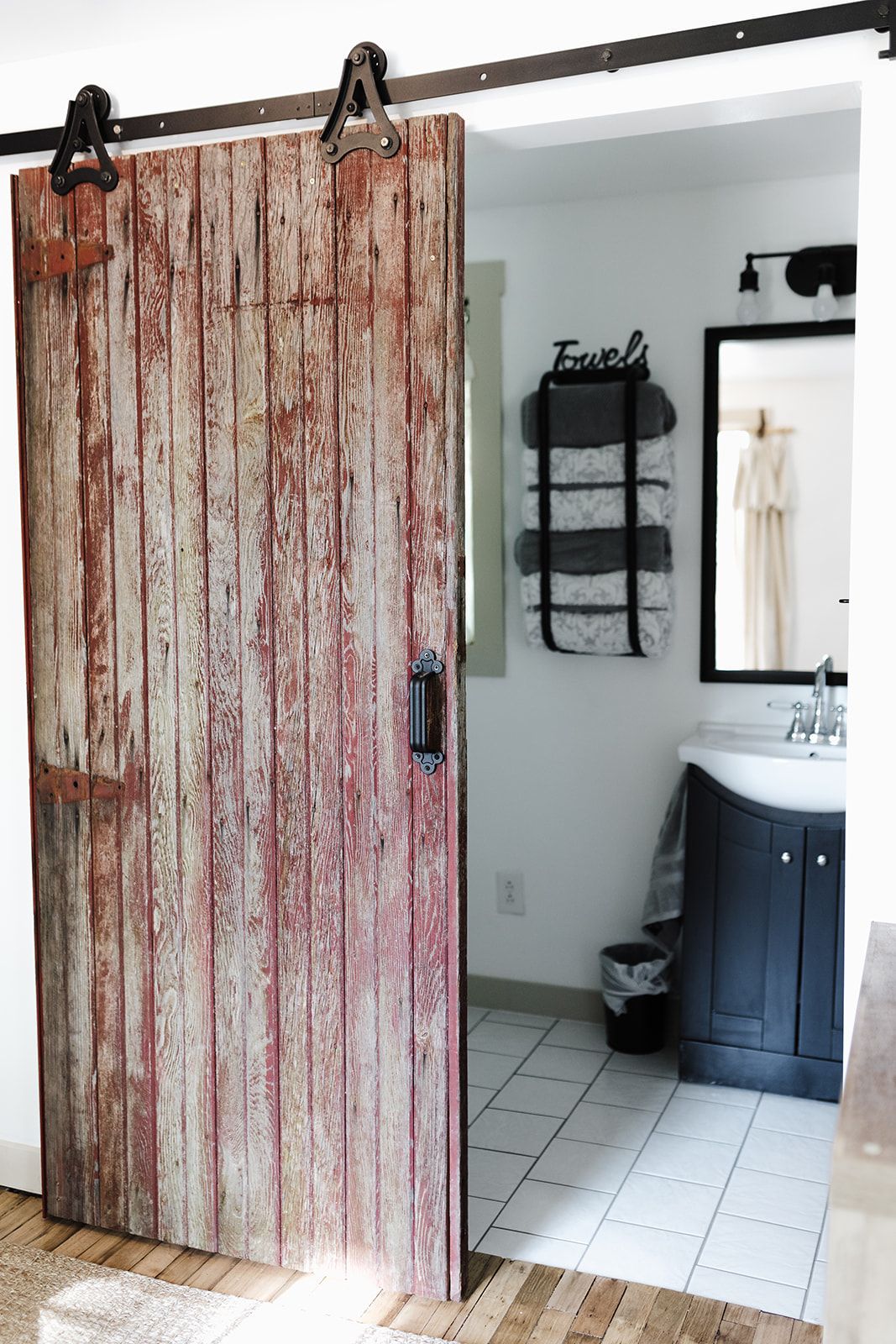 A room with a rustic wooden sliding door, a black towel rack with a towel, and a bathroom with a sink and mirror.